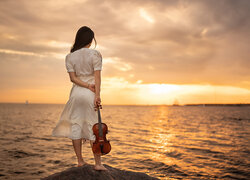 Dziewczyna ze skrzypcami nad morzem o wschodzie słońca