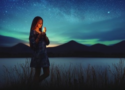 Dziewczyna ze świecą przy brzegu jeziora w nocy