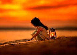 Dziewczynka bawi się na piasku w świetle lampy naftowej