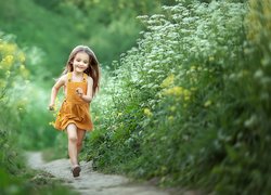 Dziewczynka biegnąca po ścieżce wśród polnych kwiatów