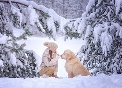 Dziewczynka i golden retriever pod ośnieżonymi choinkami