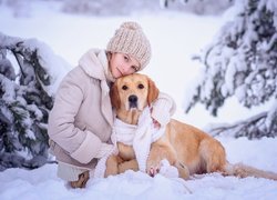 Dziewczynka i golden retriever w szaliku na śniegu