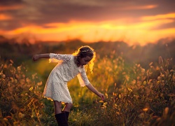 Dziewczynka na polu pośród roślinności o zachodzie słońca