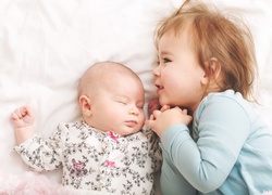 Dziewczynka przytulona do śpiącego niemowlęcia w łóżku