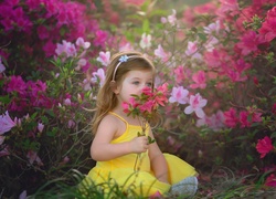 Dziewczynka siedząca na trawie z kwiatkiem w ręce