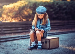 Dziewczynka siedząca na walizce obok torów kolejowych