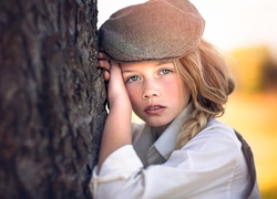 Dziewczynka w czapeczce oparta o drzewo