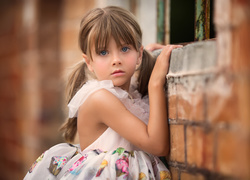 Dziewczynka w kolorowej sukience stoi przy murze