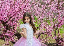 Dziewczynka w koronkowej sukience obok kwitnącego drzewa