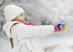 Dziewczynka w kurtce i rękawiczkach łapie płatki śniegu
