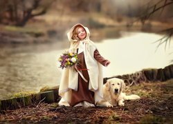 Dziewczynka w pelerynie z kwiatami i psem golden retriever