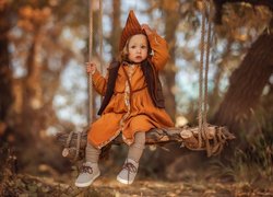 Dziewczynka w pomarańczowej sukience na huśtawce