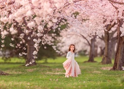 Dziewczynka w strojnej sukience pośród kwitnących drzew