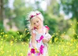 Dziewczynka w wianku zrywa polne kwiatki na łące