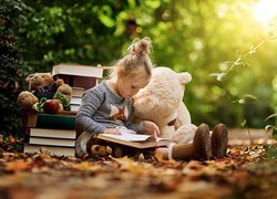 Dziewczynka z misiem czytająca książkę w lesie