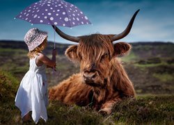 Dziewczynka z parasolką obok krowy