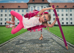 Dziewczynka z tornistrem wsparta na ołówku wykonuje akrobacje