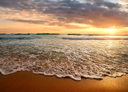 Fale morskie na plaży w blasku zachodzącego słońca