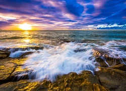 Fale morskie uderzające o kamienisty brzeg w blasku wschodzącego słońca