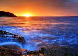 Fale na skalistym wybrzeżu morza w promieniach zachodzącego słońca