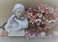 Figurka kobiety obok kwiatów
