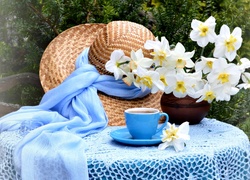 Filiżanka herbaty na stole obok kapelusza i wazonu z narcyzami
