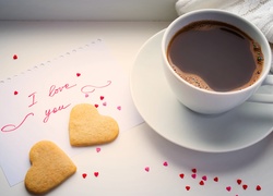 Filiżanka kawy obok ciasteczek w kształcie serca i wyznania miłosnego