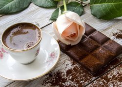 Filiżanka kawy obok róży położonej na tabliczce czekolady