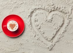 Filiżanka kawy obok serca na piasku