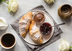 Filiżanka kawy obok talerza z rogalikami i dżemem