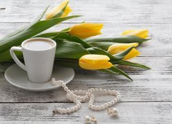 Filiżanka kawy obok tulipanów i biżuterii