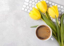 Filiżanka kawy obok żółtych tulipanów na klawiaturze