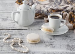 Filiżanka kawy z ciasteczkami obok naszyjnika z pereł