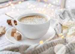 Filiżanka kawy z dwoma kostkami cukru obok swetra i lampek