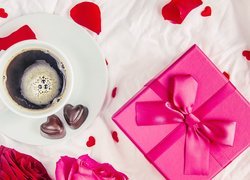 Filiżanka z kawą i czekoladkami obok prezentu wśród płatków róż