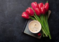 Filiżanka z kawą i czerwonymi tulipanami na książce