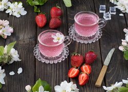 Filiżanki z napojem owocowym i truskawki wśród kwiatów