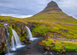 Góra Kirkjufell i wodospad Kirkjufellsfoss w Islandii pod pochmurnym niebem