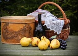 Gruszki i kiść winogron obok butelki wina i koszyka