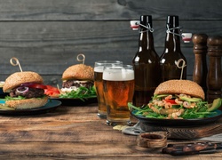 Hamburgery na talerzach obok piwa w szklankach