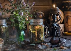 Herbata miętowa w słoiku obok kwiatów i figurki ze świecą