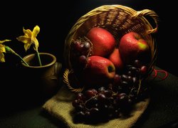 Jabłka i winogrona w koszyku obok wazonu z narcyzami