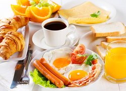 Jajka sadzone i parówki obok rogalików i szklanki soku