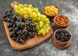 Jasne i ciemne winogrona obok miseczek z suszonymi owocami