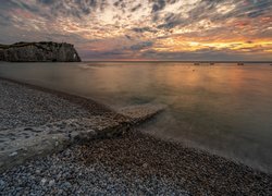Kamienista plaża na wybrzeżu Normandii o zachodzie słońca