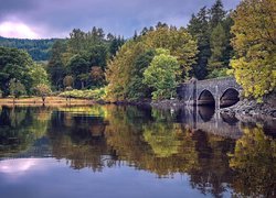 Kamienny most nad jeziorem w otoczeniu jesiennych drzew