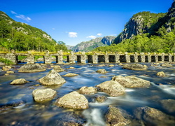 Kamienny most przez rzekę z górami w tle