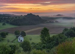 Kapliczka na łące i zamglone o poranku pola