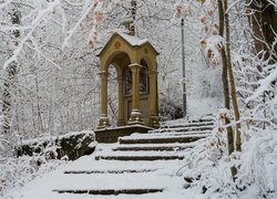 Kapliczka obok ośnieżonych schodów pod zimowymi drzewami
