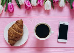 Kawa obok croissanta i telefonu przy tulipanach